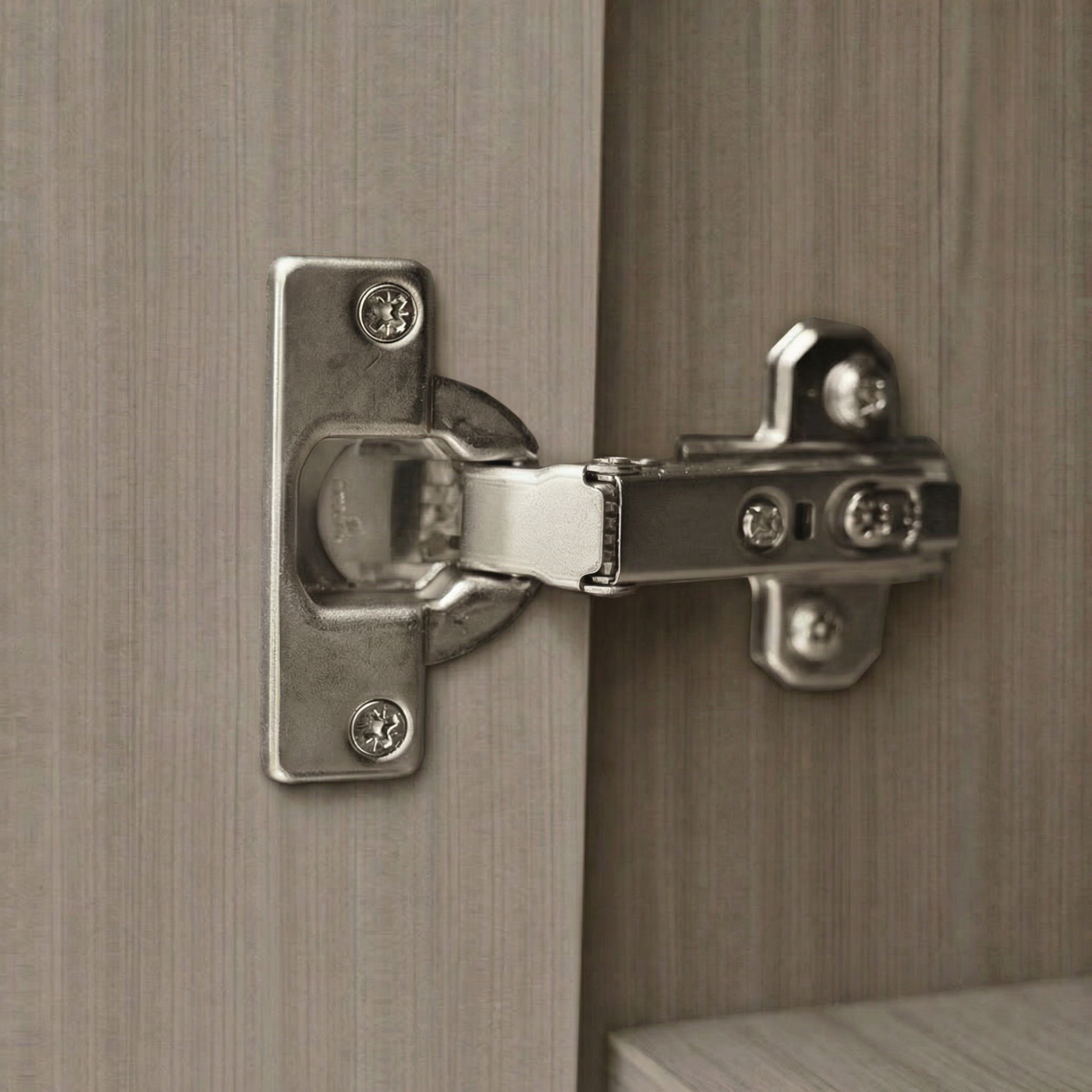 Acercamiento a bisagra metálica bidimensional de alta resistencia instalada en puerta de gabinete color ceniza.